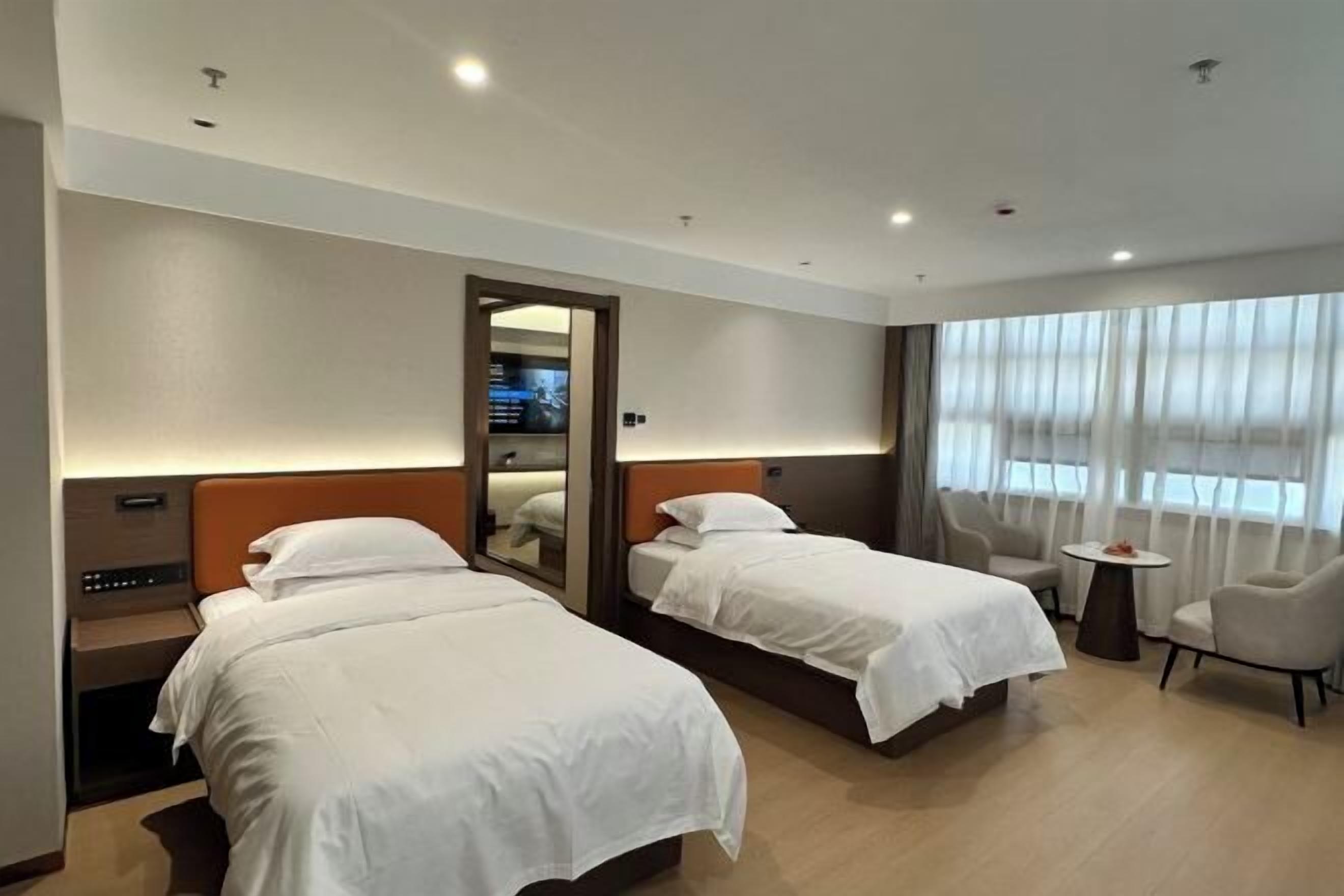 A hotel room with two beds, a small table, a chair, and a large window with curtains.