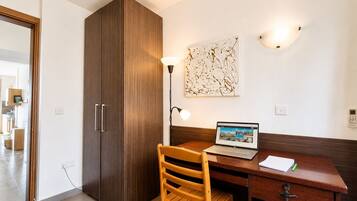 Ein Zimmer mit einem Holztisch, einem Laptop, einem Stuhl, einem Kleiderschrank und einer Wandleuchte.