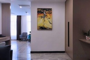 A hotel lobby with a modern design, featuring a large abstract painting on the wall, a reception desk, and a seating area with chairs. - Elegance Hotel (Suqian)