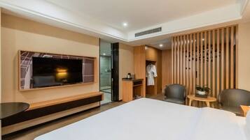 A modern hotel room with a large bed, a TV mounted on the wall, a seating area with chairs, and a small table with a plant.
