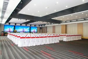 Un salón de conferencias con filas de sillas blancas, una pantalla grande y piso alfombrado.