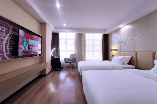 A hotel room with two beds, a TV on the wall, a desk, and a chair.
