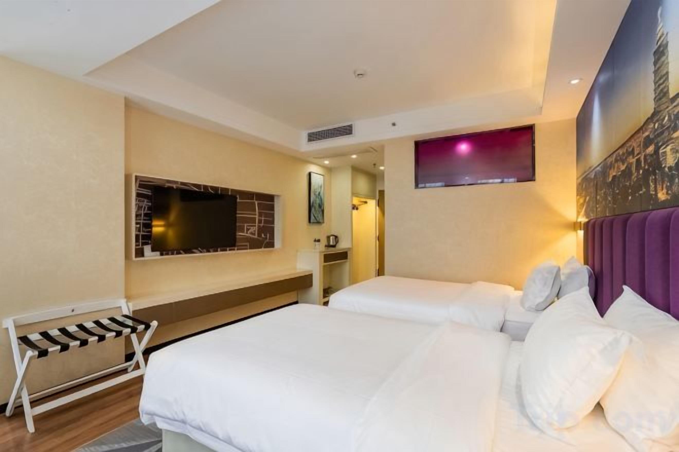 Habitación de hotel con una cama grande, televisión montada en la pared y una pequeña zona de estar con un banco.