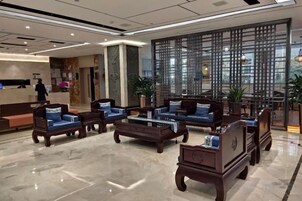 Vestíbulo de hotel con disposición de asientos, una mesa de recepción y un separador decorativo.