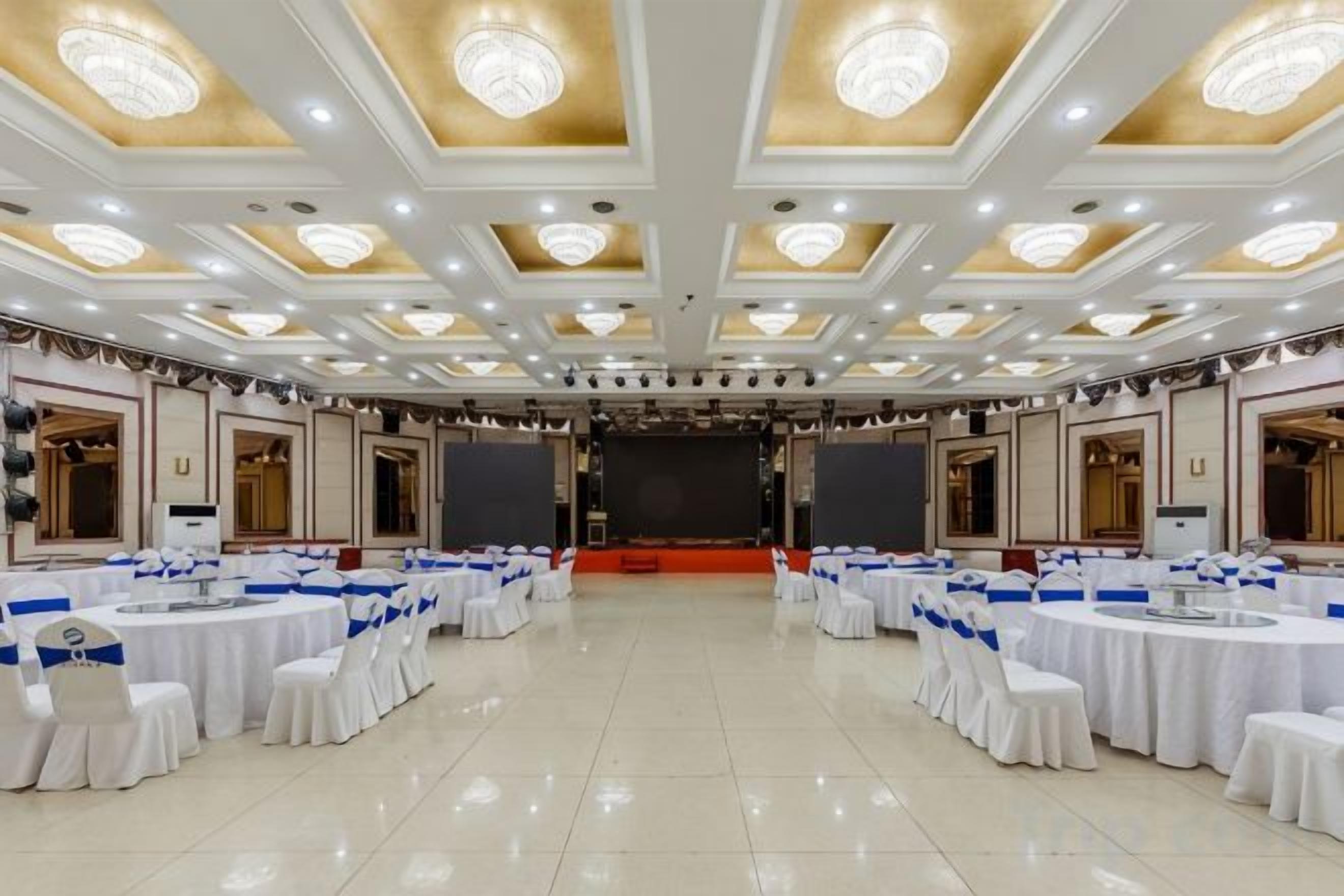 Un salón de banquetes con mesas y sillas redondas, un escenario y una araña.
