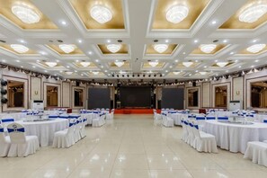 A banquet hall with round tables and chairs, a stage, and a chandelier. - Elegance Hotel (Suqian)