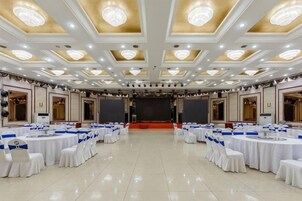 Un salón de banquetes con mesas y sillas redondas, un escenario y una araña.