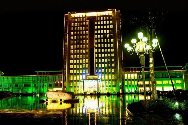 A high-rise building with a reflective pool in front, a boat, and a street lamp.