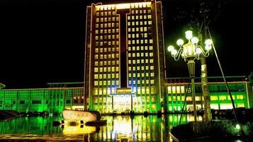 A high-rise building with a reflective pool in front, a boat, and a street lamp.
