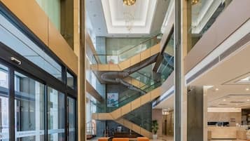 Un atrio de varios niveles con barandillas de vidrio, una escalera central y una zona de recepción.