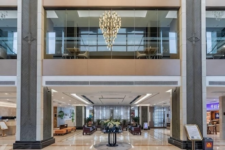 A spacious lobby with a chandelier, seating areas, and a view of the upper floor.. Elegance Hotel