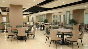 A spacious indoor area with multiple seating arrangements, including round tables and chairs, and a large window providing natural light.