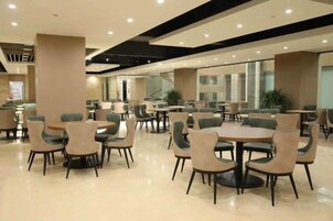 Un espacio interior amplio con diversas opciones de asientos, incluidas mesas redondas y sillas, y un gran ventanal que proporciona luz natural.