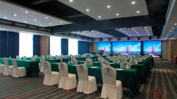 A conference room with rows of tables and chairs, large windows, and a cityscape view.