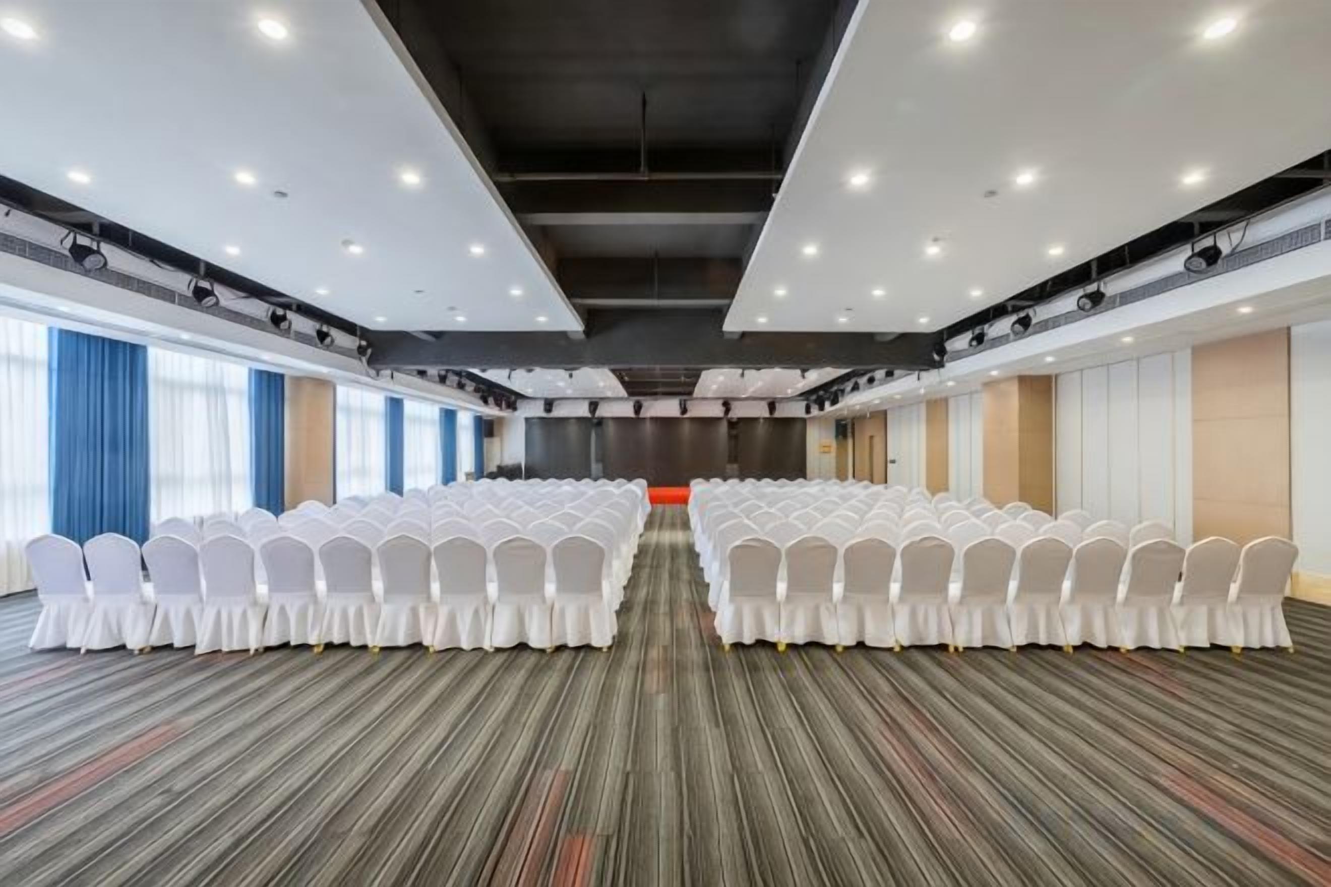 Un salón de conferencias con filas de sillas blancas, piso alfombrado y un gran ventanal en un lateral.