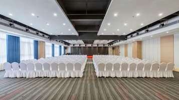 Un salón de conferencias con filas de sillas blancas, piso alfombrado y un gran ventanal en un lateral.