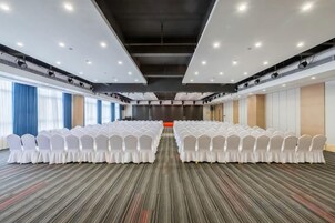 Un salón de conferencias con filas de sillas blancas, piso alfombrado y un gran ventanal en un lateral.