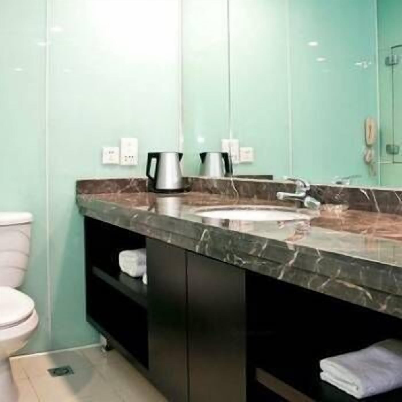 A bathroom with a marble countertop, a sink, a toilet, and a mirror.