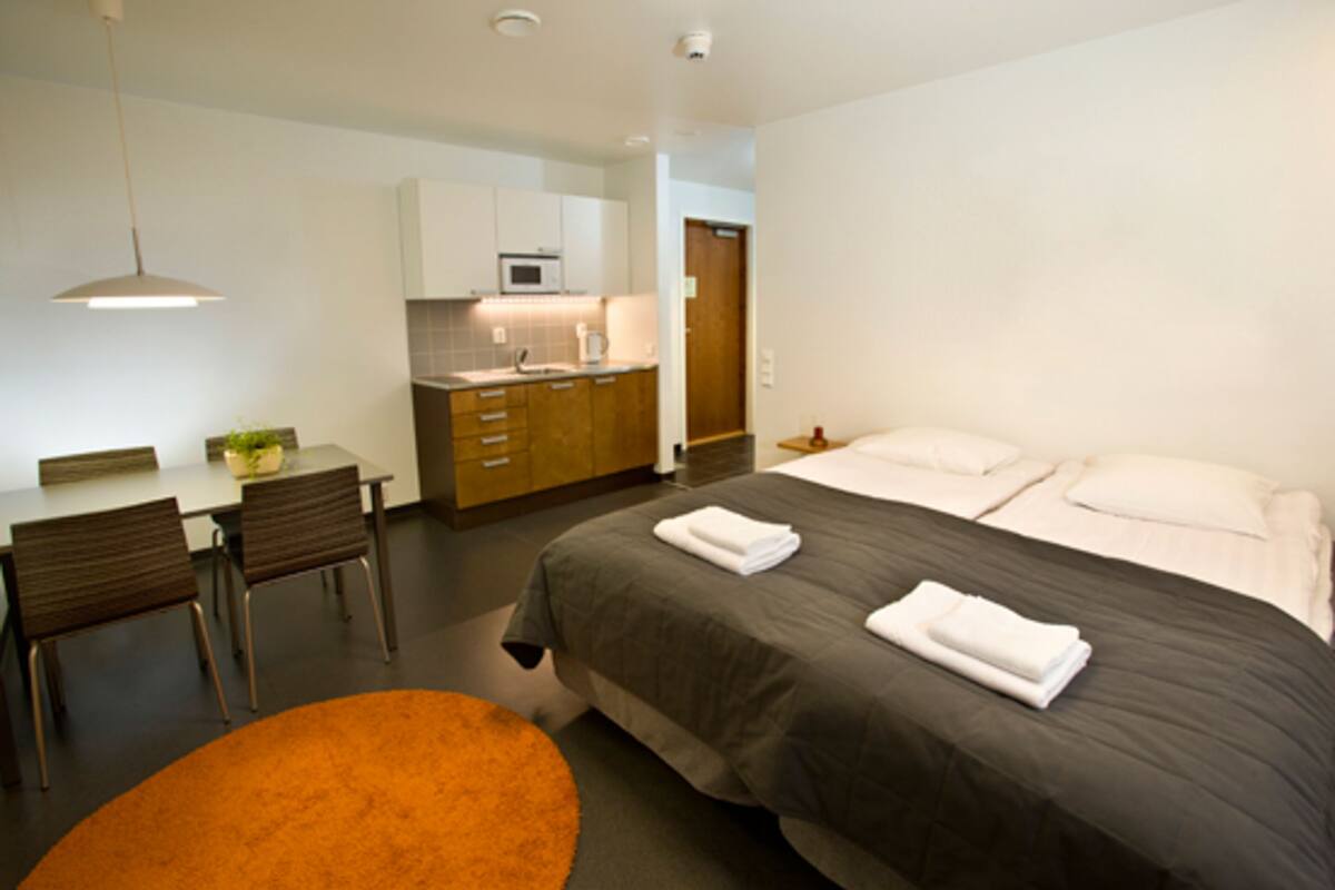 A modern hotel room with a bed, a desk, and a kitchenette.