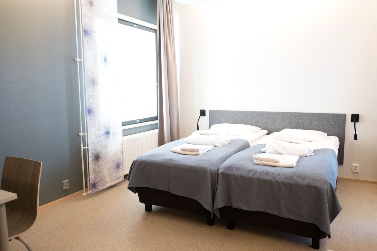 A hotel room with two beds, a chair, and a window with curtains.