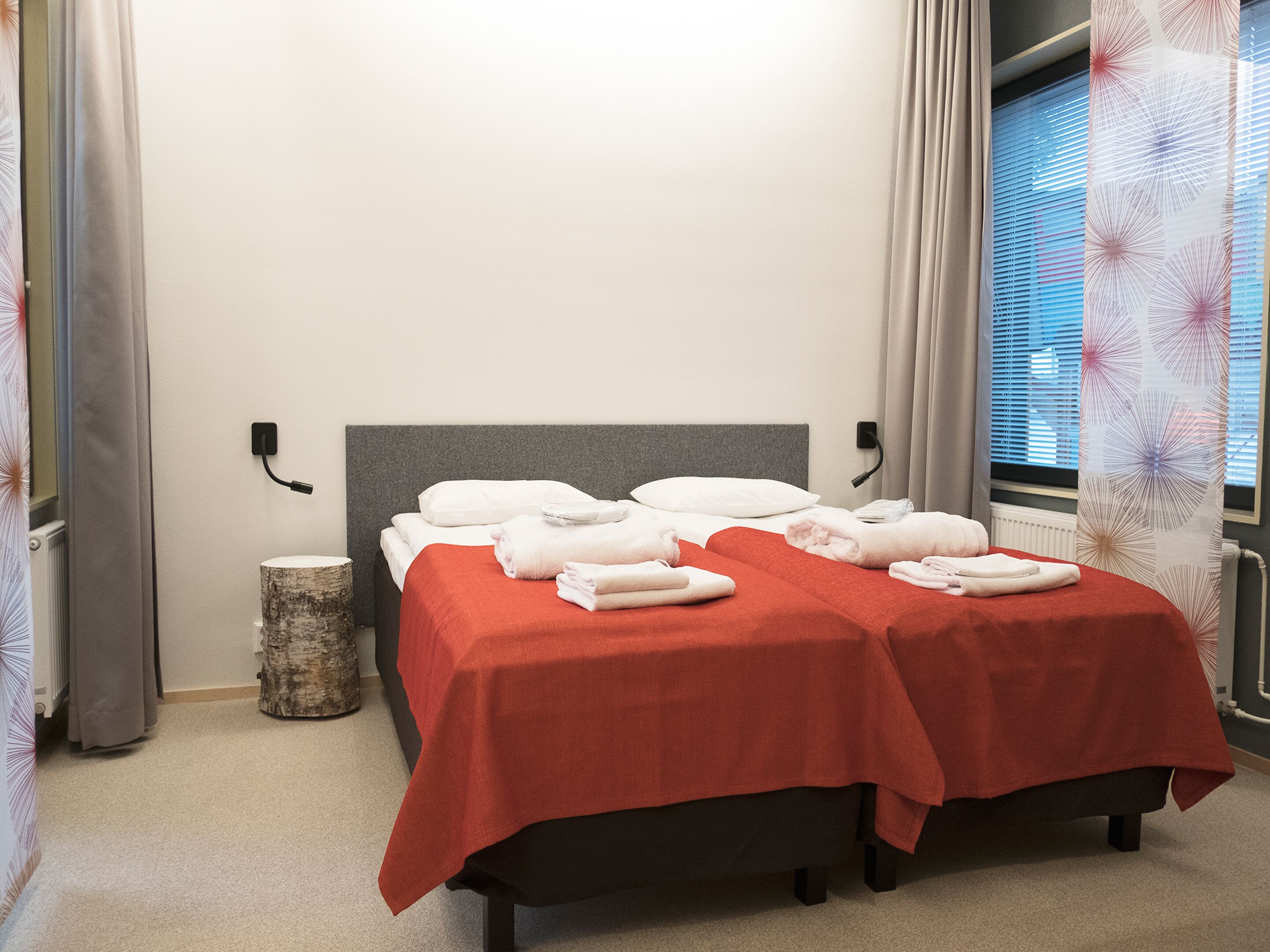 Ein Hotelzimmer mit zwei Betten, jeweils mit roter Decke, weißen Kissen und ordentlich gefalteten Handtüchern.
