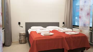 Ein Hotelzimmer mit zwei Betten, jeweils mit roter Decke, weißen Kissen und ordentlich gefalteten Handtüchern.