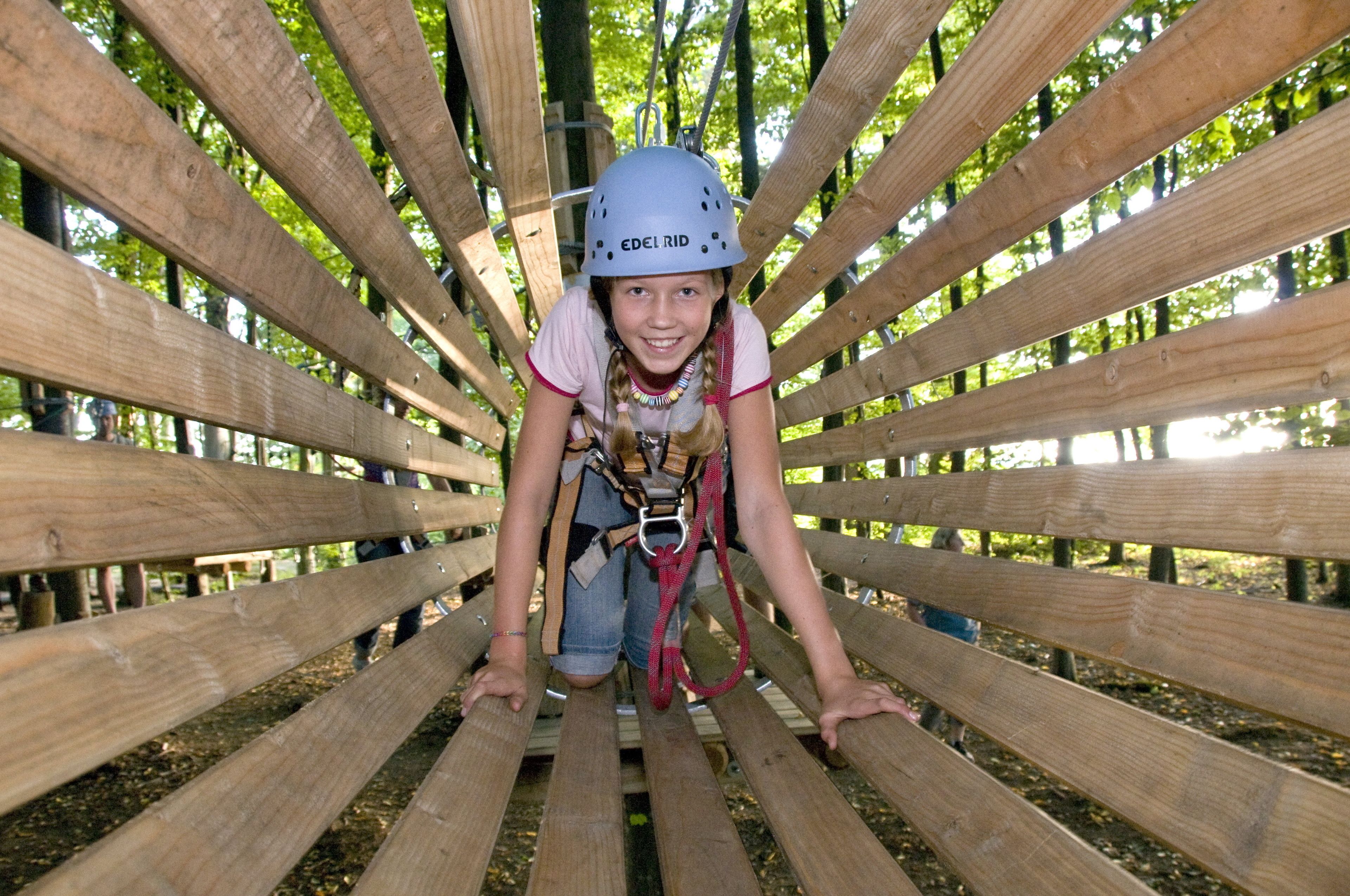 A person in a helmet and harness on a wooden bridge structure.
