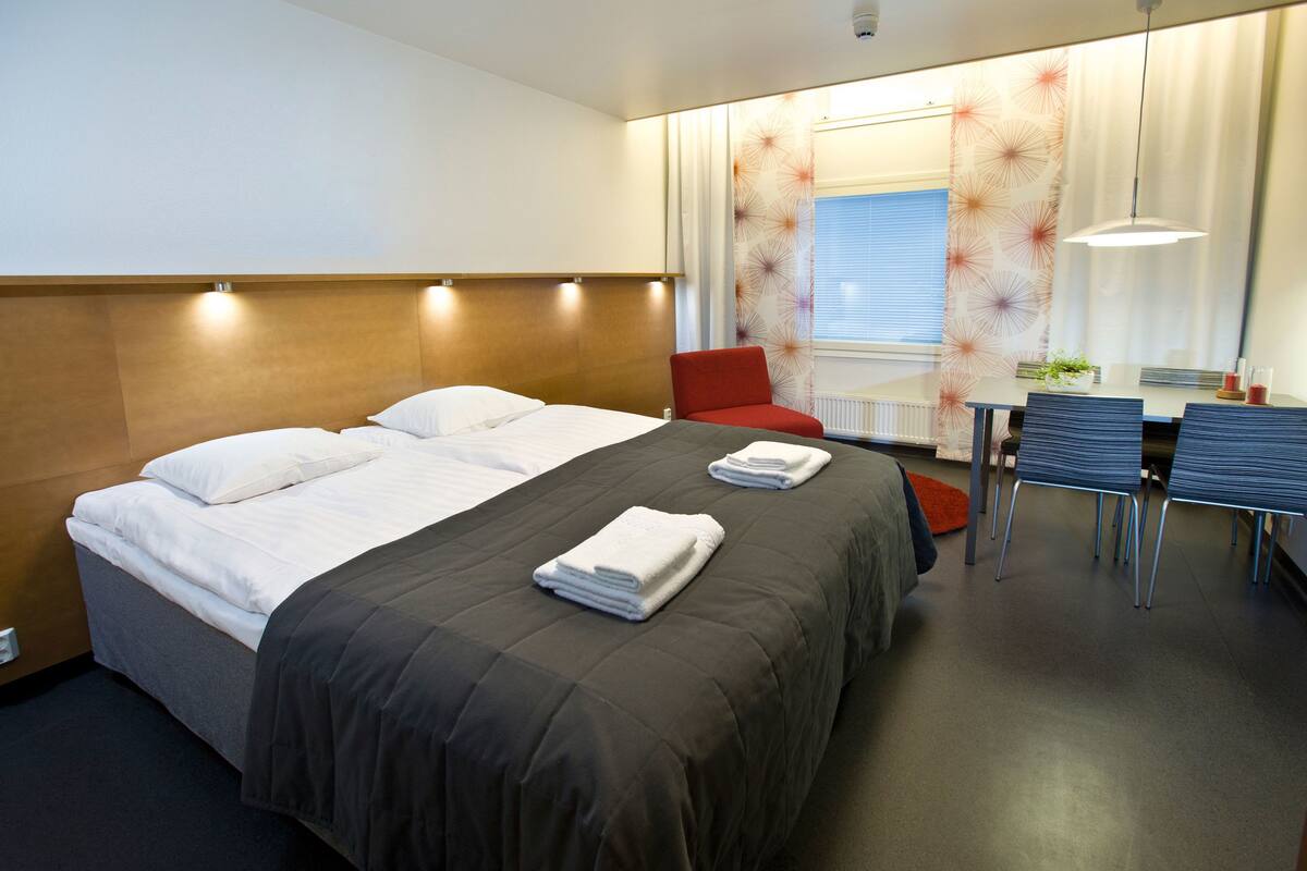 A hotel room with a large bed, a dining table with chairs, and a red armchair.