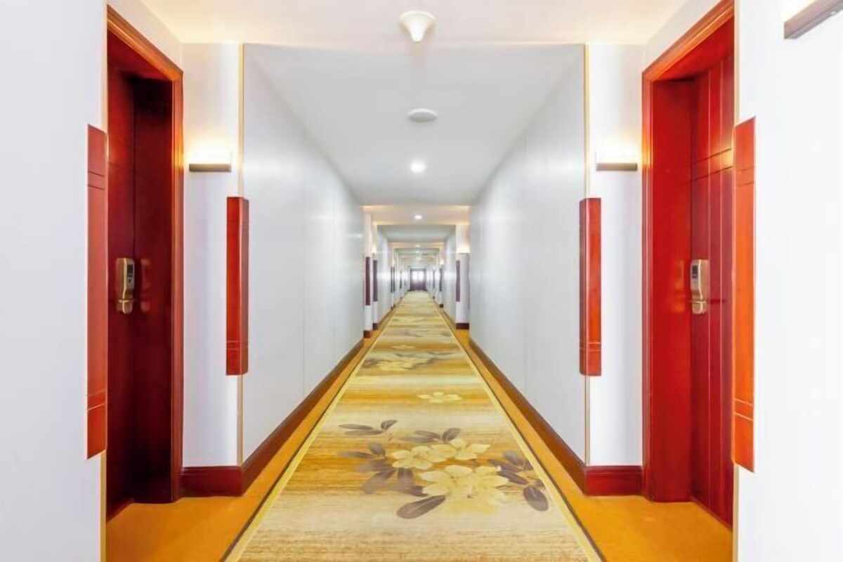 A long, narrow hotel corridor with red doors on either side and a carpeted floor.