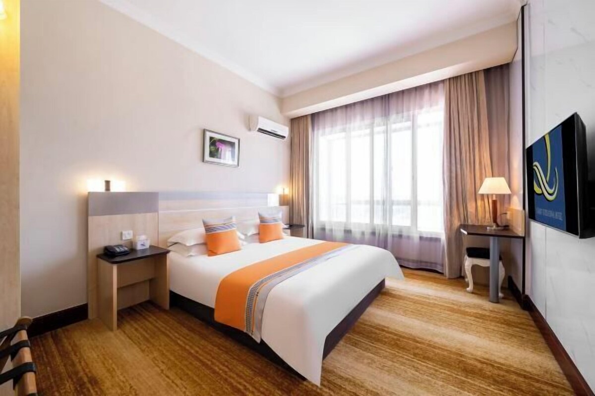 A hotel room with a bed, bedside table, lamp, and a TV on the wall.