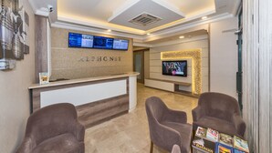 A reception area with a reception desk, a digital display, a television, and two armchairs. - Alphonse Hotel (Istanbul)