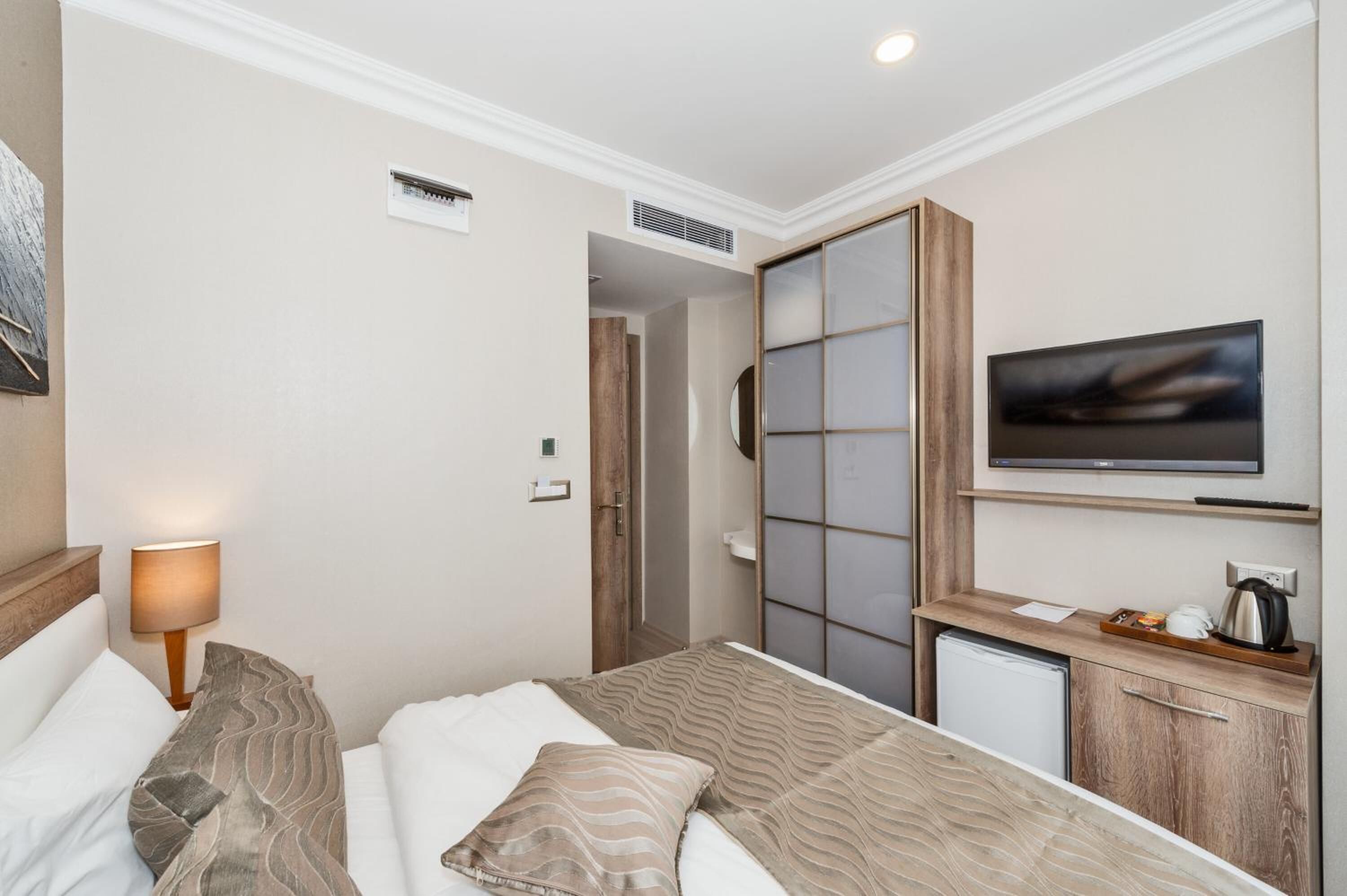 A hotel room with a bed, a TV, a small kitchenette, and a sliding door closet.