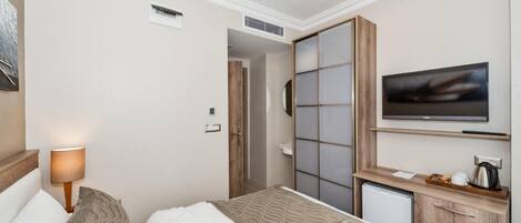 Una habitación de hotel con cama, televisor, kitchenette pequeño y armario con puerta corredera.