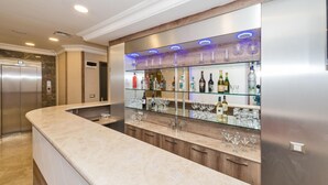 A modern bar area with a curved countertop, glass shelves displaying bottles and glasses, and a stainless steel refrigerator. - Alphonse Hotel (Istanbul)