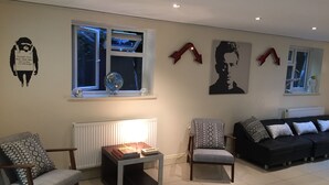 A living room with a sofa, two armchairs, a coffee table, and a radiator. There are two windows with curtains, a globe, and wall art.