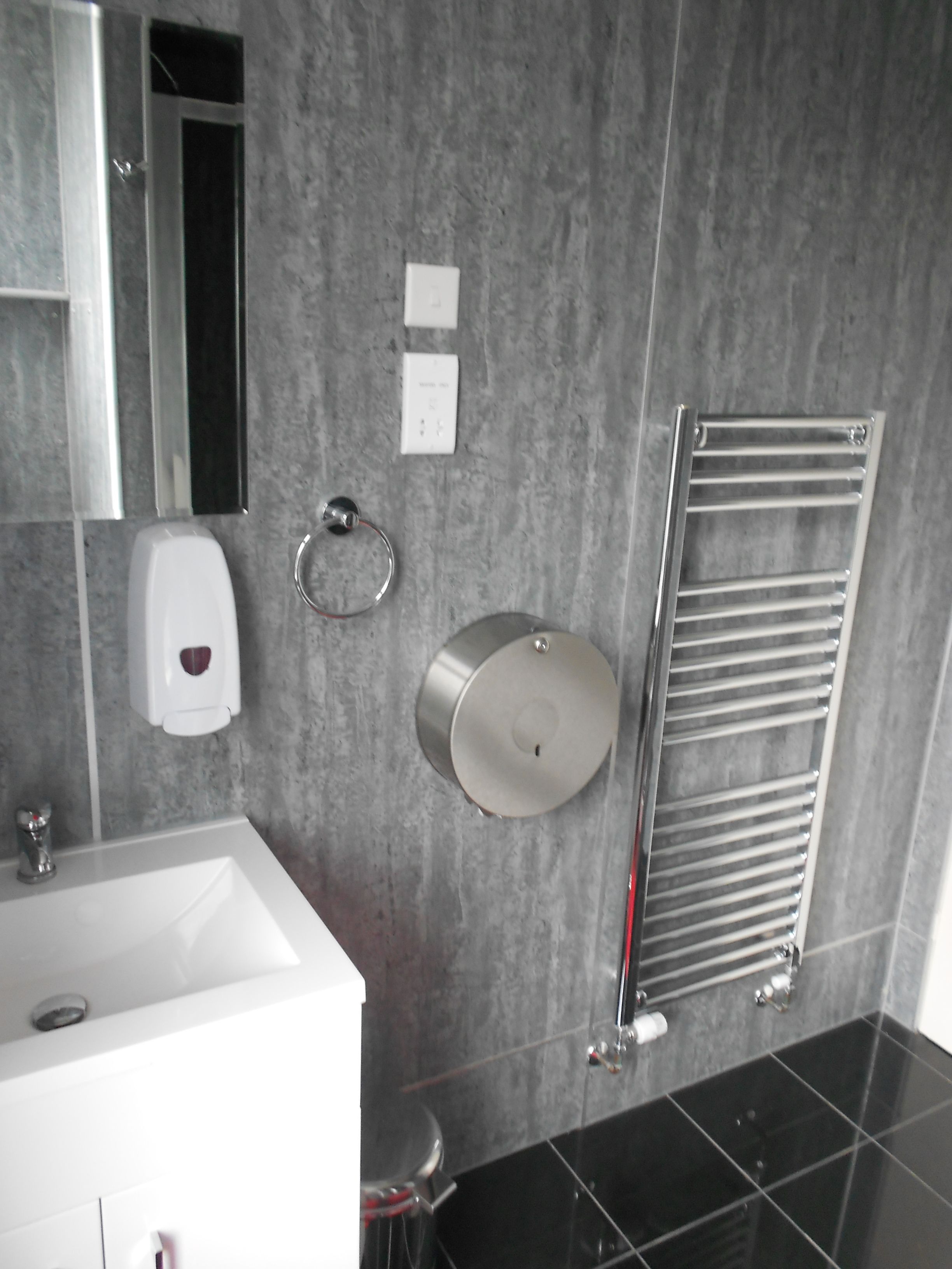 A modern bathroom with a white sink, a mirror, a towel rack, and a hand dryer.