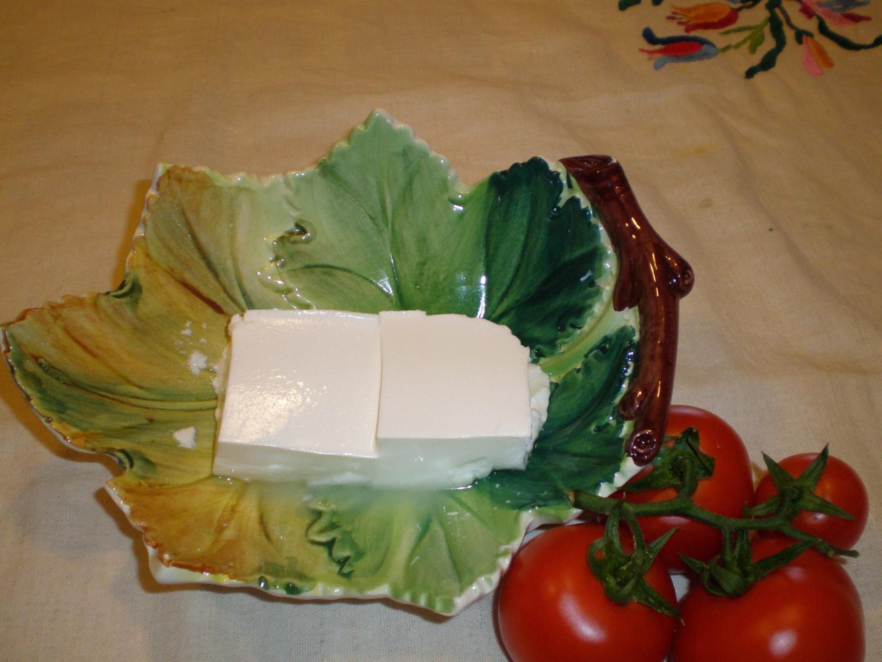 A plate with a block of cheese, a bunch of cherry tomatoes, and a leafy vegetable on a tablecloth.