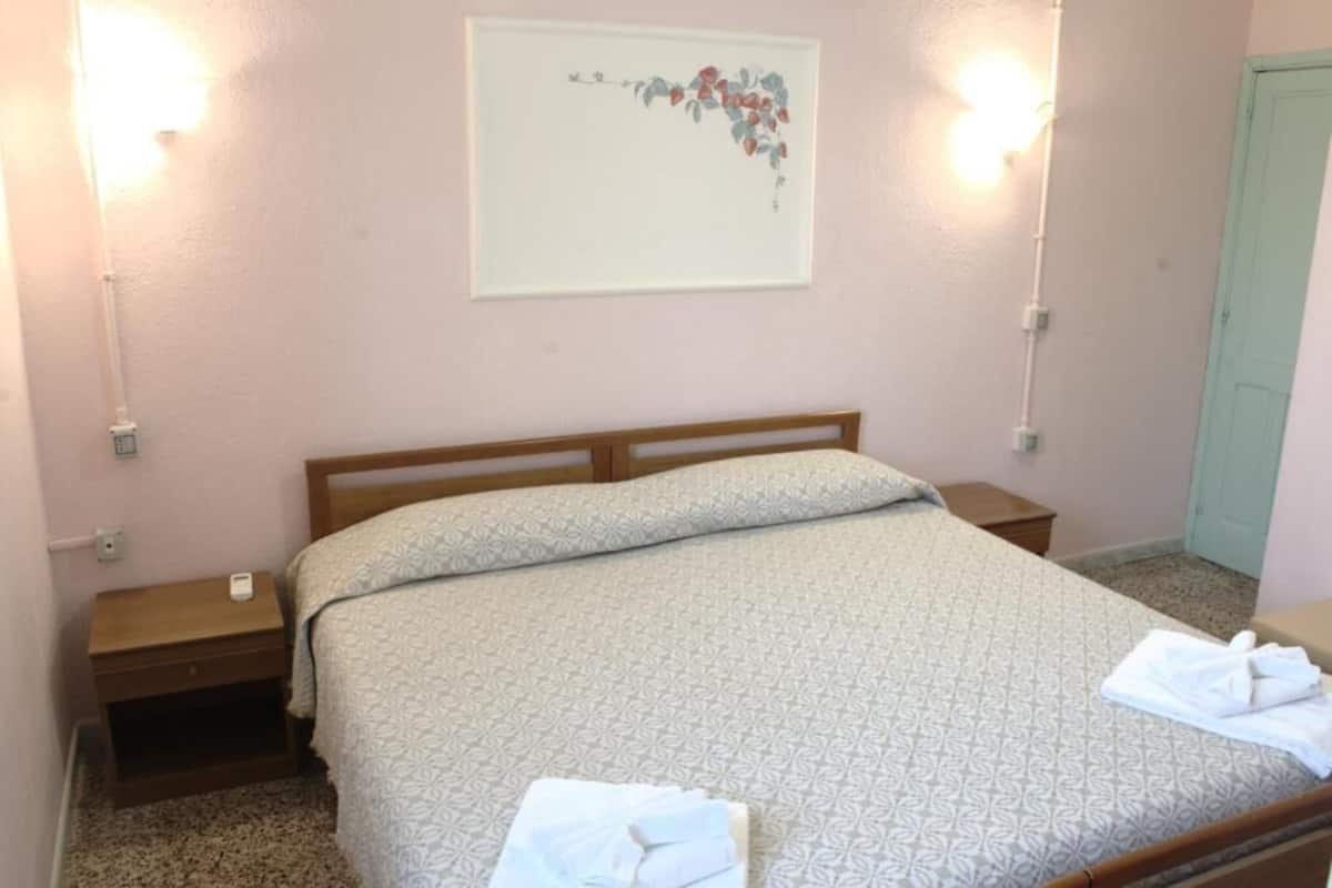 Un dormitorio con cama, dos mesitas de noche, un tocador y un cuadro enmarcado en la pared, además de una puerta.