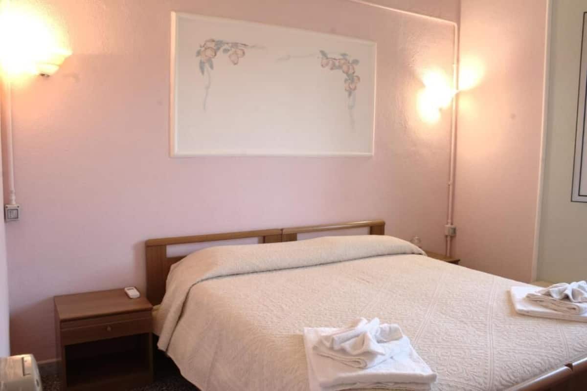 Una habitación de hotel con cama, mesita de noche, lámpara de pared y un cuadro enmarcado.