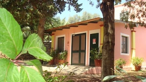 A building with a pink facade, green doors, and potted plants in the foreground. - Agriturismo Menhir (Villagrande Strisaili)