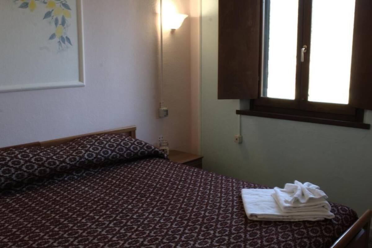 Un dormitorio con una colcha estampada, una lámpara de noche, una ventana con cortinas y una obra de arte colgada en la pared.