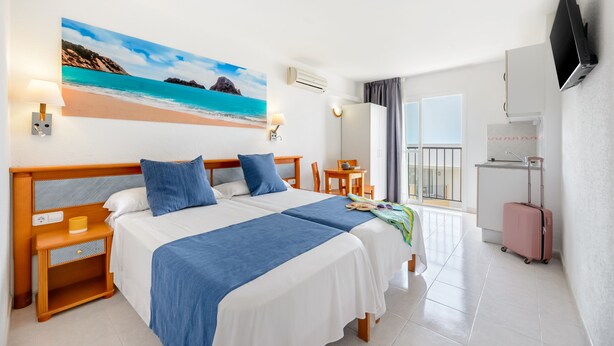 Una habitación de hotel con dos camas, un escritorio, una silla, un televisor y un balcón.
