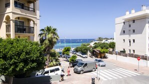 Un edificio costero con balcones que dan al mar, coches estacionados y cielo despejado.