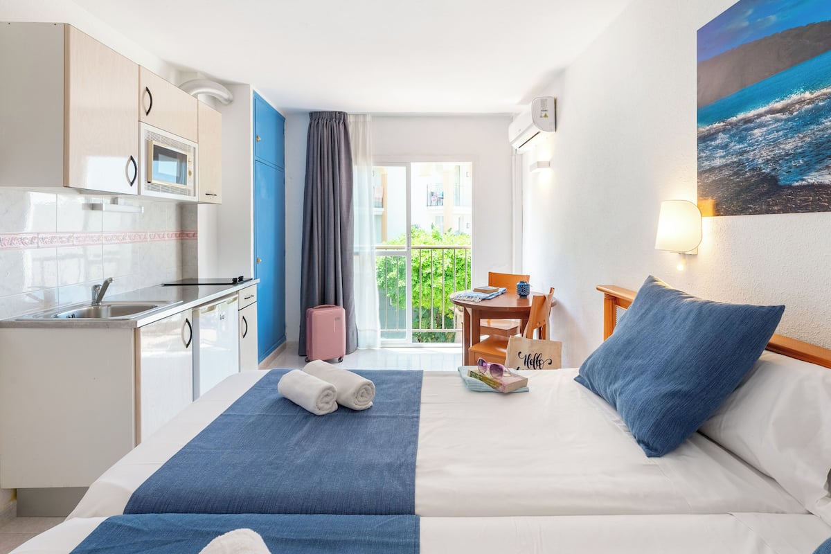 Een hotelkamer met een bed, een bureau, een kitchenette en een balkon met uitzicht.