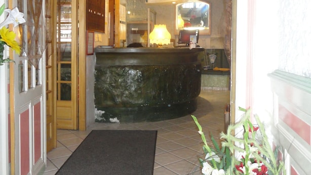 A hotel lobby with a reception desk, a large decorative fountain, and a potted plant with flowers. - Hôtel Saint Christophe (Lourdes)