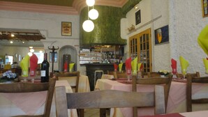 A restaurant interior with wooden tables and chairs, a bar area with bottles and glasses, and a sign indicating the presence of whiskey. - Hôtel Saint Christophe (Lourdes)