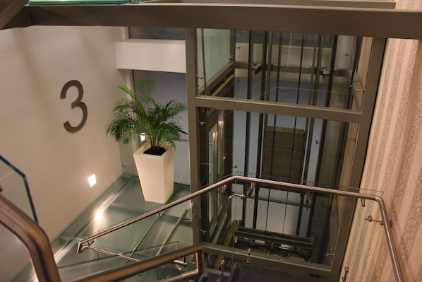 A modern interior with a glass railing, a potted plant, and a large number '3' on the wall.