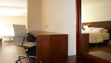 Een hotelkamer met een houten bureau, een witte bureaustoel, een bed met witte lakens en een nachtkastje.