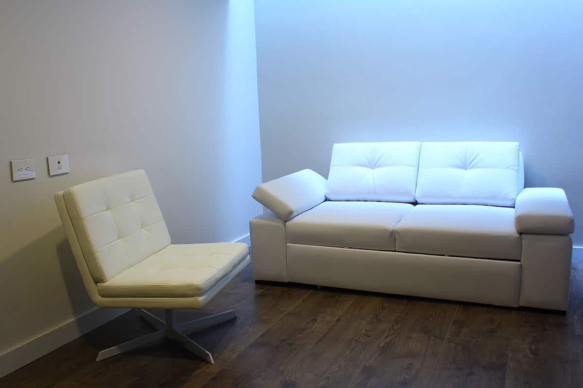 A room with a white leather chair and a white sofa against a plain wall.