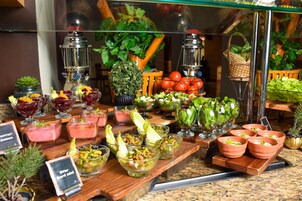 Buffet com diversos alimentos e bebidas, incluindo saladas, frutas e refrigerantes.